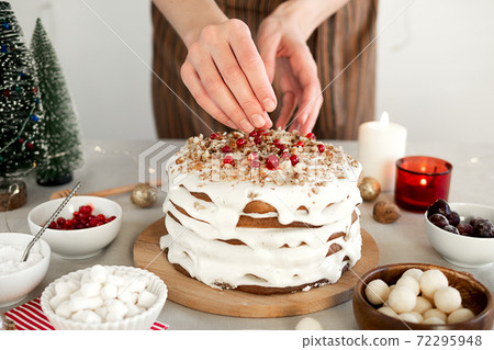 Preparing food for Christmas dinner. Women's hands are decorated with berries a homemade Christmas cake with white icing sugar, nuts and red cranberries Preparing food for Christmas dinner. Women's hands are decorated with berries a homemade Christmas cake with white icing sugar, nuts and red cranberries 72295948