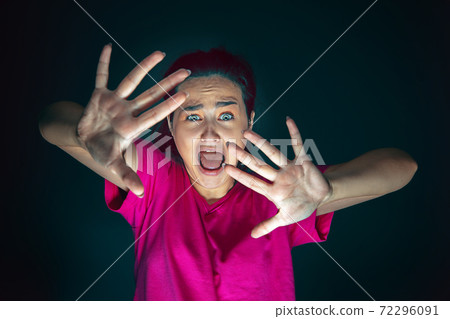 Close up portrait of young crazy scared and shocked woman isolated on dark background Close up portrait of young crazy scared and shocked woman isolated on dark background 72296091