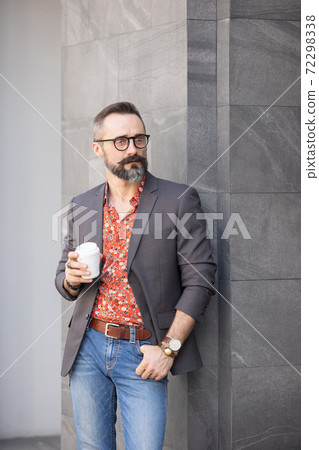 Handsome cheerful man standing near office building holding disposable cup coffee Handsome cheerful man standing near office building holding disposable cup coffee 72298338
