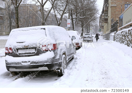 City after blizzard. Cars parked on a street covered with snow. City after blizzard. Cars parked on a street covered with snow. 72300149