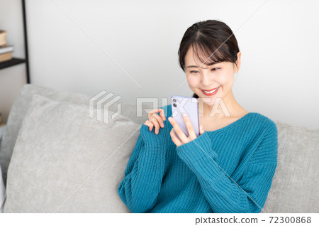 一個年輕的女人坐在客廳裡的沙發上,使用智能手機 一個年輕的女人坐在客廳裡的沙發上,使用智能手機 72300868