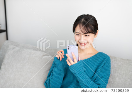 一個年輕的女人坐在客廳裡的沙發上,使用智能手機 一個年輕的女人坐在客廳裡的沙發上,使用智能手機 72300869