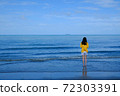 Back side of a girl in yellow shirt standing in the sea looking at the horizon. 72303391