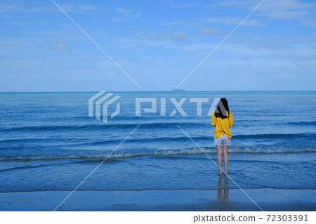 Back side of a girl in yellow shirt standing in the sea looking at the horizon. 72303391