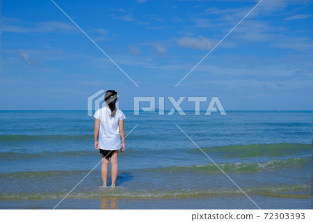 Back side of a girl standing in the sea looking at the horizon. 72303393