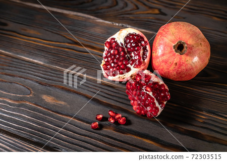 Craked ripe pomegranate on dark wooden background Craked ripe pomegranate on dark wooden background 72303515