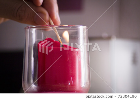 Fingers of man lighting a red candle inside a glass vase with a match Fingers of man lighting a red candle inside a glass vase with a match 72304190