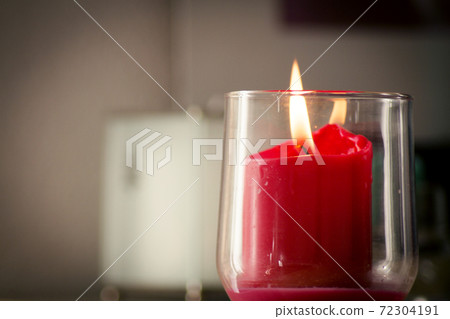 Burning red candle inside a clear glass vase Burning red candle inside a clear glass vase 72304191