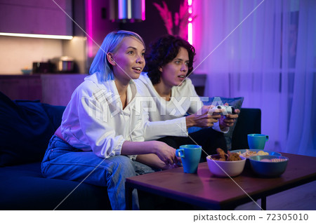 Handsome young man teaching how to play the video games to his girlfriend, on the couch, concept about home entertainment, video games. 72305010