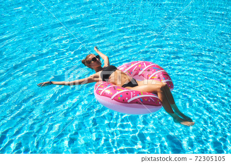 Beautiful young woman swimming on pink donut swim ring in pool 72305105