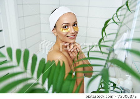 Portrait of a young woman in a bathroom with patches under the eyelids Portrait of a young woman in a bathroom with patches under the eyelids 72306872