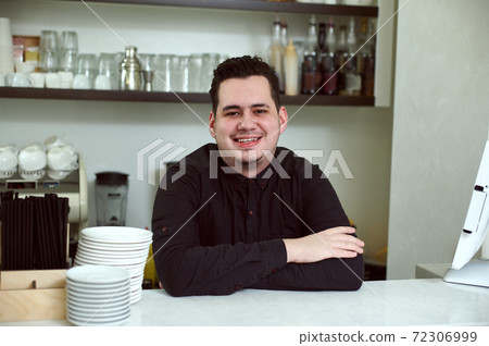 An arms crossed handsome man smiling at the camera behind the bar An arms crossed handsome man smiling at the camera behind the bar 72306999