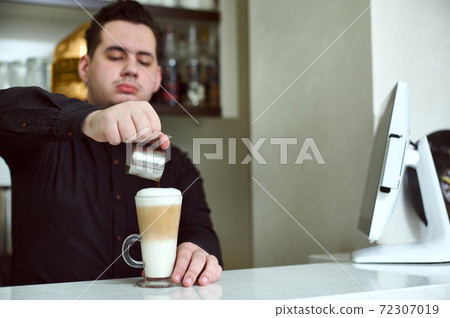 Barista pours coffee into a glass with a latte. Focus on preparation latte 72307019