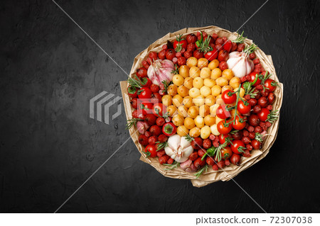 Large bouquet created of smoked cheese, sausages, tomato, pepper and garlic wrapped in craft paper. Top view on black background Large bouquet created of smoked cheese, sausages, tomato, pepper and garlic wrapped in craft paper. Top view on black background 72307038