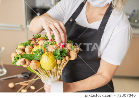 Female designer finishes assembling a fruit bouquet for a gift Female designer finishes assembling a fruit bouquet for a gift 72307040
