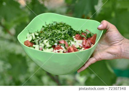 Vegetable salad of tomatoes and cucumbers in a green bowl on a green background 72307348
