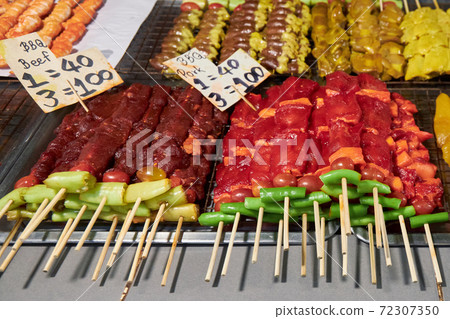 Different kind of meats on barbecue skewers are on the counter in a market in Thailand 72307350