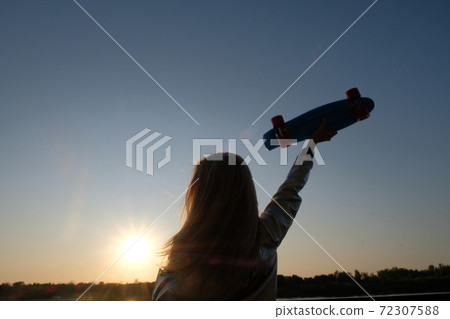 Silhouette of the woman with pennyboard in her raised hand 72307588
