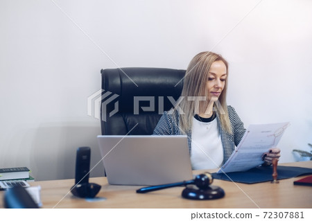 Female lawyer sitting in the office and and reading documents. 72307881