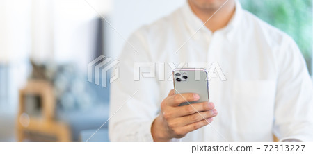 Banner size of a young man operating a smartphone in the living room 72313227
