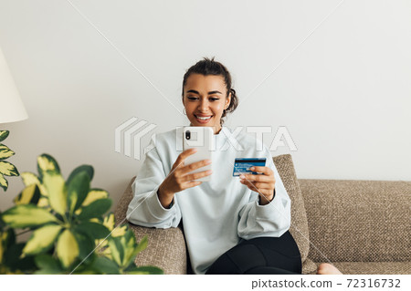 Smiling woman using smartphone and credit card. Young female making a purchase online. Smiling woman using smartphone and credit card. Young female making a purchase online. 72316732