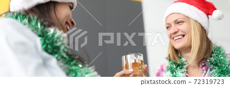 Two women friends in santa claus hats hold glasses of whiskey with ice in their hands in apartment 72319723
