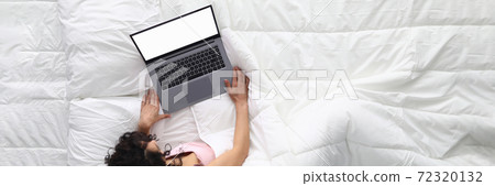 Woman lies on white bed with laptop. 72320132