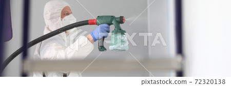 Man in protective suit and respirator sprays paint on walls. 72320138