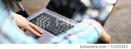 Woman in wheelchair on her knees stands laptop in park Woman in wheelchair on her knees stands laptop in park 72320163