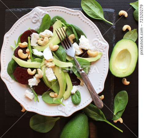Healthy beet salad with fresh sweet baby spinach, nuts, feta cheese and avocado. Plate with salad  on dark table. Top view 72320279