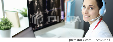 Medical officer is at computer wearing headphones and holding an X-ray Medical officer is at computer wearing headphones and holding an X-ray 72320531