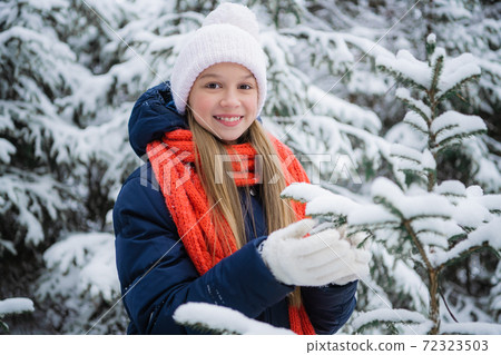 A young teenage girl in a down jacket smiles beautifully for a picture in a winter snow covered forest 72323503