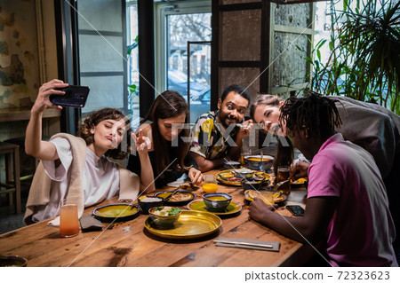 Five young friends sitting at the table in a cafe, taking selfie 72323623