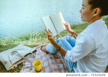 Women sitting a relax River side in the park. sitting working with a notebook and drinking coffee. in the holiday 72324209