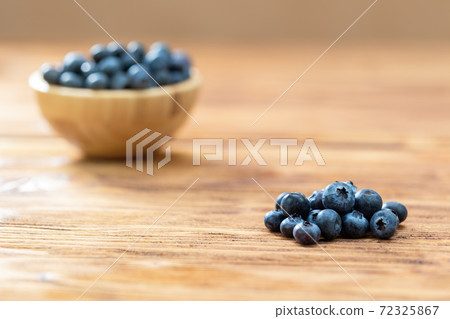 Pile of fresh blueberries with full wooden bowl on desk 72325867