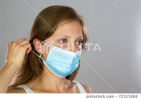 Female model in white shirt attaching surgical face mask on light background Female model in white shirt attaching surgical face mask on light background 72325868