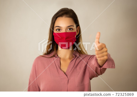 Positive young woman with red mask with thump up in studio 72325869