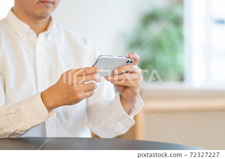 Hands of a young man looking at a smartphone in the living room 72327227