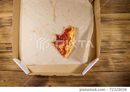 Bitten slice of pizza in cardboard box on a wooden table. Top view. Concept for home delivery of food, fast food, delivery of pizza Bitten slice of pizza in cardboard box on a wooden table. Top view. Concept for home delivery of food, fast food, delivery of pizza 72328036