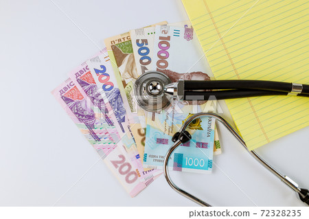 Stethoscope phonendoscope on a Ukrainian money grivna with banknotes on yellow notebook write in the white background 72328235