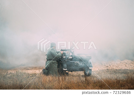 Re-enactor Dressed As World War II German Soldier Open Fire Near Motorcycle. Historical Reenactment Re-enactor Dressed As World War II German Soldier Open Fire Near Motorcycle. Historical Reenactment 72329686