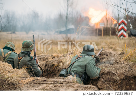 Re-enactors Dressed As German Wehrmacht Infantry Soldiers In World War II Hidden Sitting With Rifles Weapons In An Ambush In Trench Re-enactors Dressed As German Wehrmacht Infantry Soldiers In World War II Hidden Sitting With Rifles Weapons In An Ambush In Trench 72329687