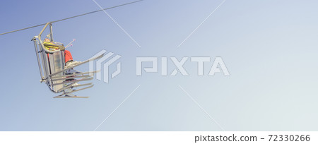 Banner with big group of skiers in ski lift, going uphill in a ski resort at blue and yellow clean gradient sky during sunset with copy space for text. 72330266