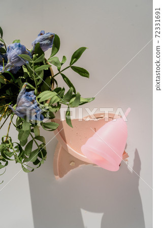 pink menstrual cup with flowers on white background with sunlight and shadows 72331691