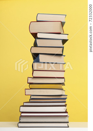 Pile of books stacked on a yellow background with space for copy in a vertical image Pile of books stacked on a yellow background with space for copy in a vertical image 72332000