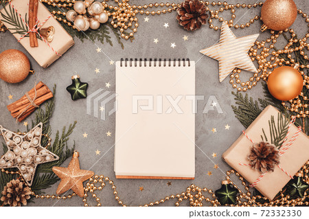 Notepad with holiday decorations in green and golden colors on grey concrete backdrop, copyspace. Christmas and New Year planning flatlay concept. Craft giftboxes, balls and stars. 72332330