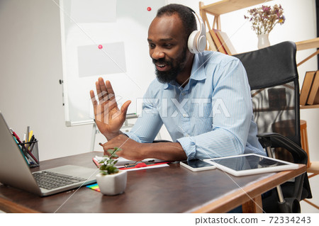 Online english courses at home. Smiling man teaches students remotely in interior of living room Online english courses at home. Smiling man teaches students remotely in interior of living room 72334243