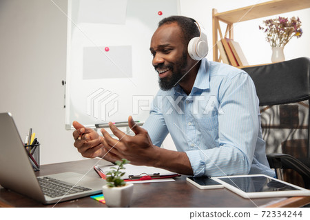 Online english courses at home. Smiling man teaches students remotely in interior of living room 72334244