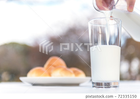 Breakfast scenery pouring milk from a pitcher into a glass on a terrace table 72335150