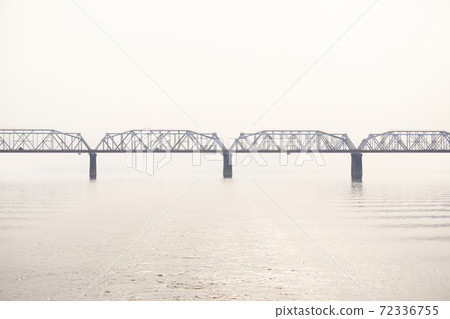 railroad truss bridge over a wide river in fog 72336755